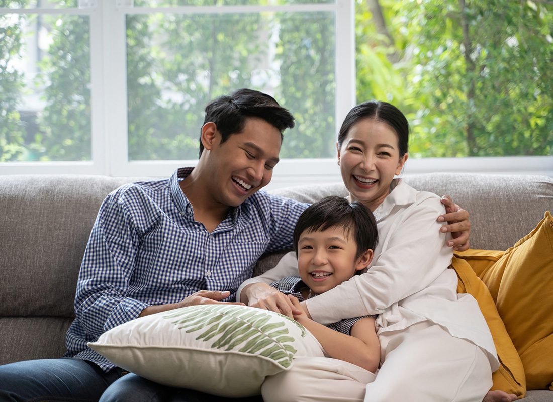 Personal Insurance - Portrait of a Cheerful Young Father and Mother Sitting with Their Young Son on the Sofa in the Living Room